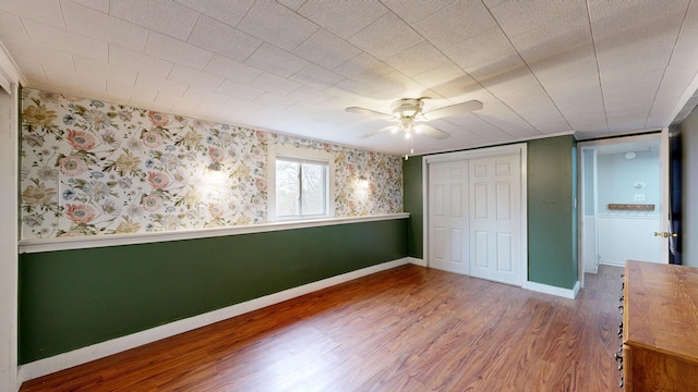 unfurnished bedroom featuring wallpapered walls, wood finished floors, baseboards, and a closet