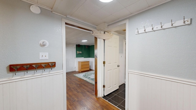 hall with dark wood-type flooring, wainscoting, and a textured wall