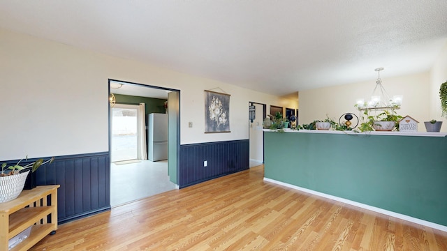 spare room featuring light wood finished floors, a notable chandelier, and a wainscoted wall