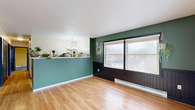 unfurnished room with a wainscoted wall, wood finished floors, and baseboard heating