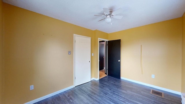 unfurnished bedroom featuring dark wood-style flooring, baseboards, a ceiling fan, and visible vents