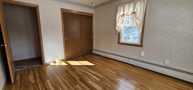 unfurnished bedroom featuring a closet, wood finished floors, baseboard heating, and wallpapered walls