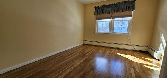 spare room featuring a baseboard heating unit, baseboards, and wood finished floors