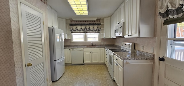 kitchen with white appliances, white cabinetry, dark stone counters, and a sink