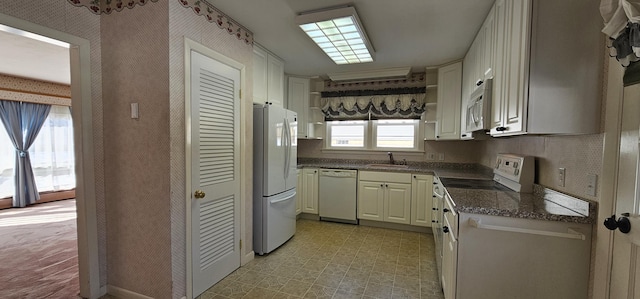 kitchen with white appliances, a sink, dark stone counters, light floors, and wallpapered walls