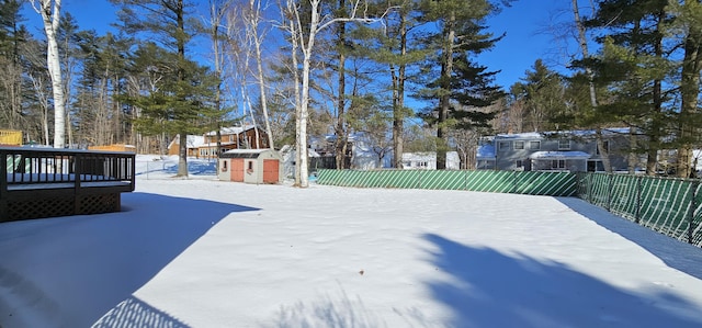 snowy yard with a storage unit, an outdoor structure, fence, and a wooden deck