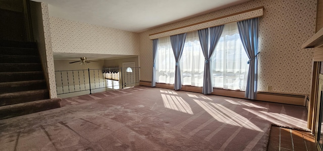 unfurnished living room with carpet, stairway, a ceiling fan, a baseboard heating unit, and wallpapered walls