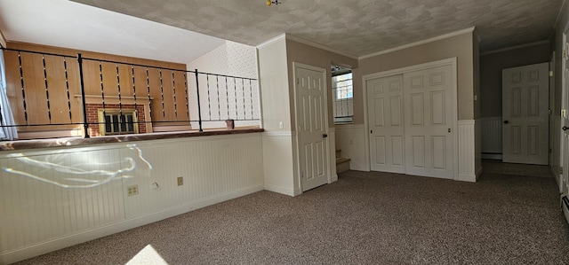 carpeted spare room featuring a baseboard radiator, a wainscoted wall, crown molding, and a textured ceiling