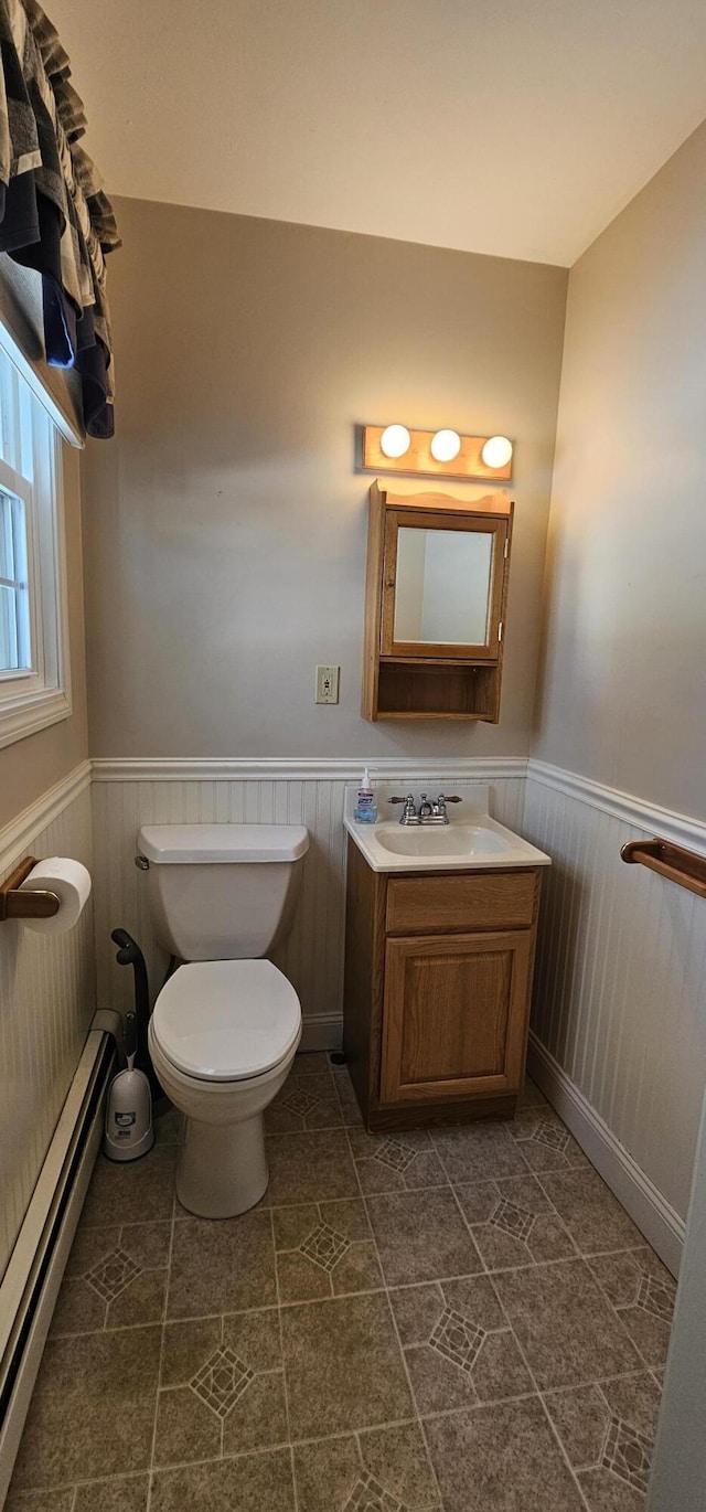 bathroom with toilet, vanity, baseboard heating, and wainscoting