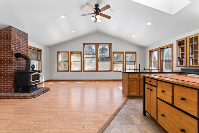 kitchen with dark countertops, open floor plan, light wood-style floors, lofted ceiling, and a wood stove