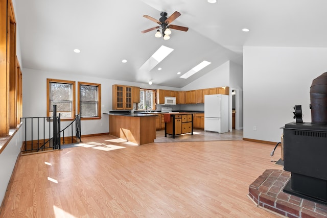 kitchen with a skylight, a wood stove, brown cabinetry, plenty of natural light, and white appliances