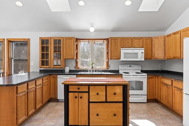 kitchen featuring glass insert cabinets, lofted ceiling with skylight, a peninsula, white appliances, and a sink