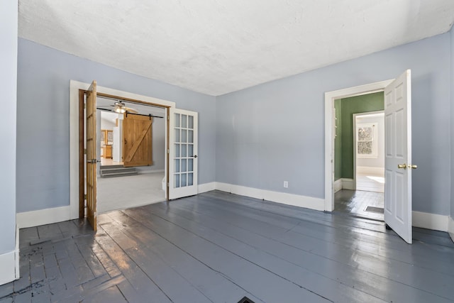 unfurnished room with dark wood-style floors, baseboards, and a barn door