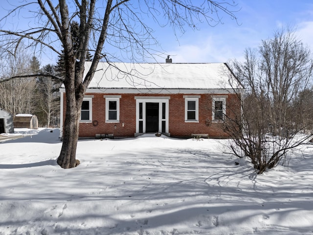 snow covered property featuring brick siding and a chimney