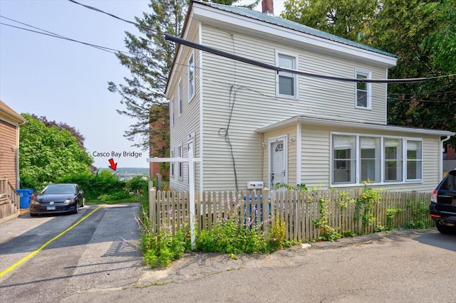 view of front of property featuring uncovered parking, metal roof, fence, and a chimney