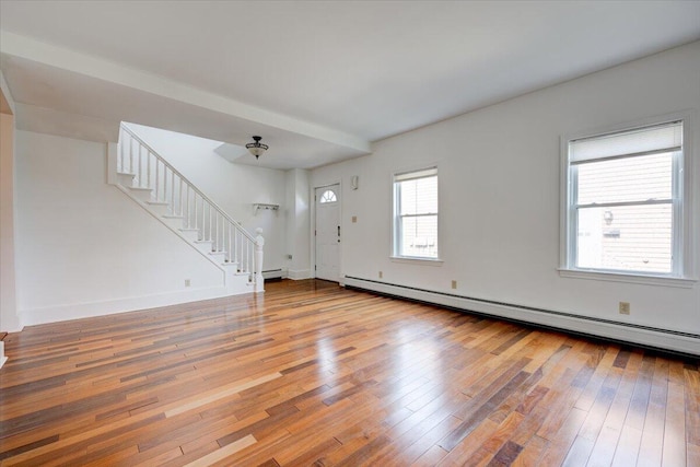 unfurnished living room with a baseboard heating unit, light wood-type flooring, stairway, and baseboards