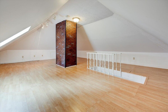 additional living space with vaulted ceiling with skylight, a textured ceiling, and wood finished floors