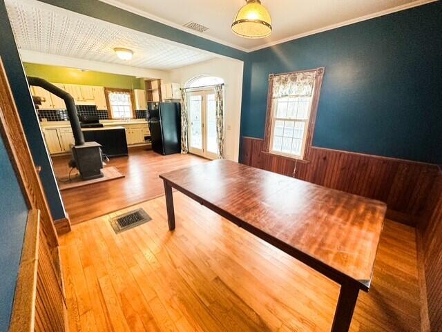 unfurnished dining area featuring visible vents, wainscoting, wood finished floors, a wood stove, and french doors