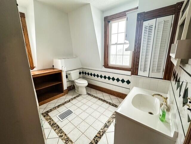 bathroom with tile patterned flooring, toilet, a wainscoted wall, vanity, and visible vents