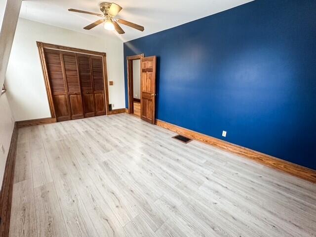 unfurnished bedroom featuring a closet, visible vents, a ceiling fan, wood finished floors, and baseboards