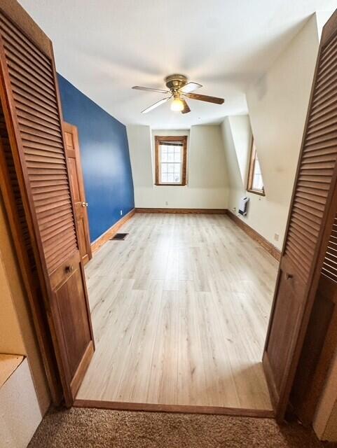 additional living space with light wood finished floors, ceiling fan, visible vents, and baseboards