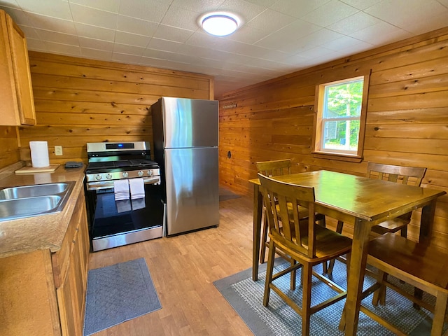 kitchen featuring stainless steel appliances, light countertops, wood walls, a sink, and light wood-type flooring