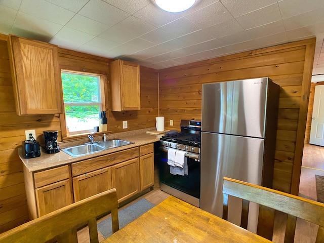 kitchen featuring wooden walls, appliances with stainless steel finishes, light countertops, and a sink