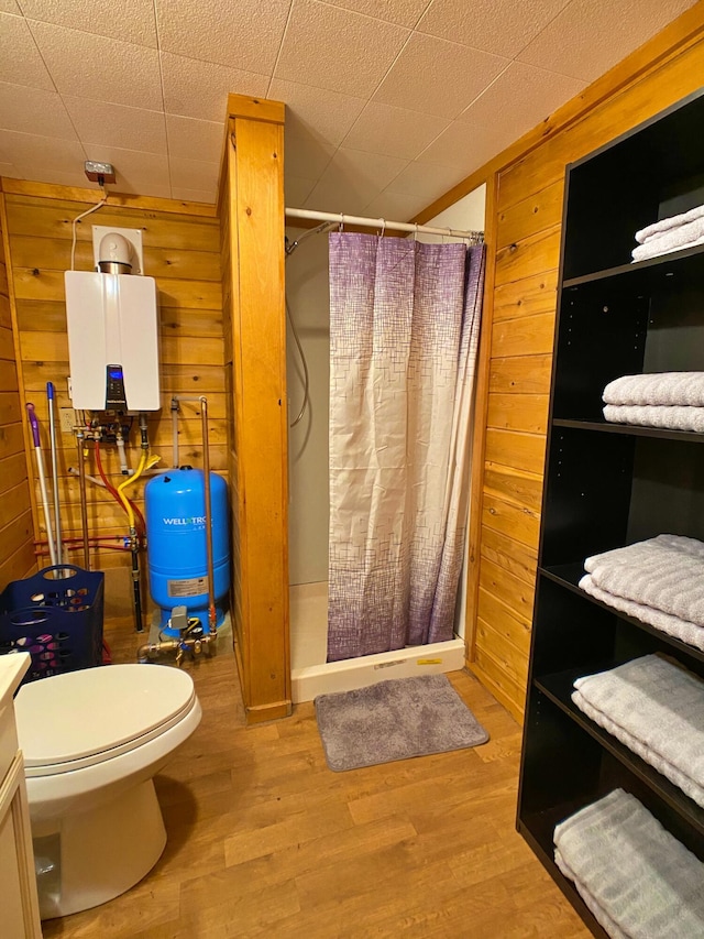 bathroom featuring wooden walls, water heater, wood finished floors, and a stall shower