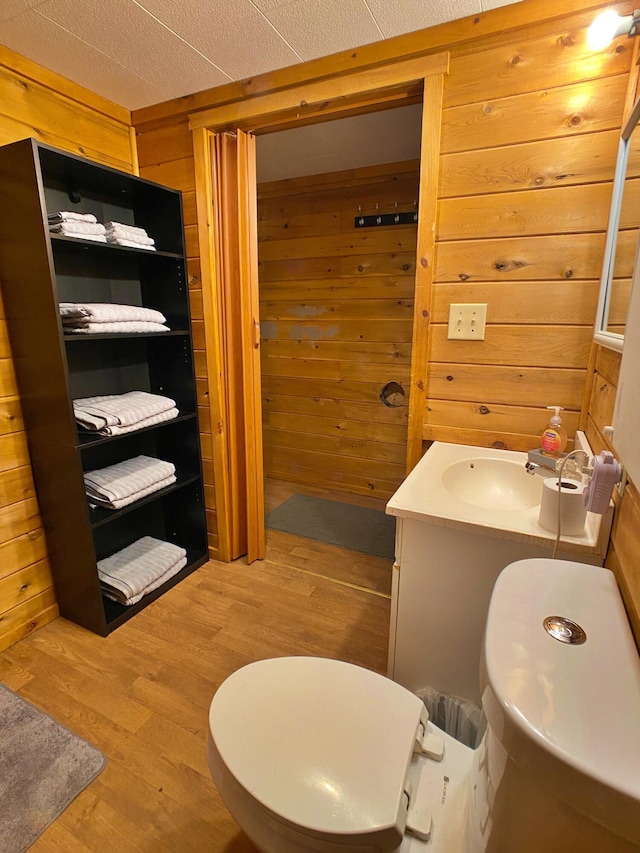 bathroom with vanity, wood finished floors, toilet, and wooden walls