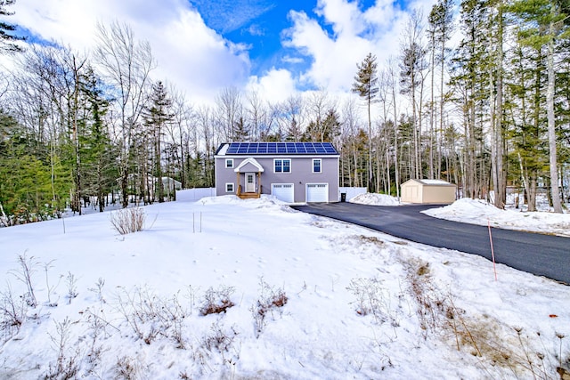 exterior space featuring aphalt driveway, a garage, an outdoor structure, roof mounted solar panels, and a shed