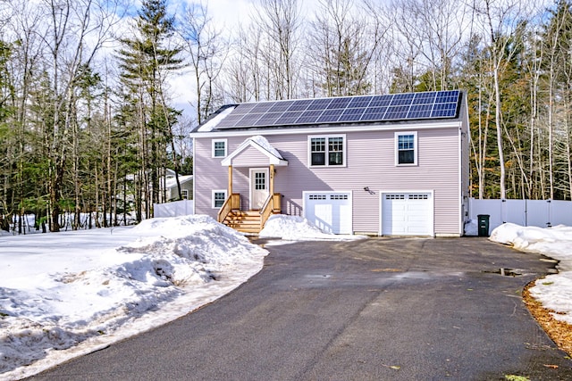 bi-level home with aphalt driveway, an attached garage, fence, and roof mounted solar panels