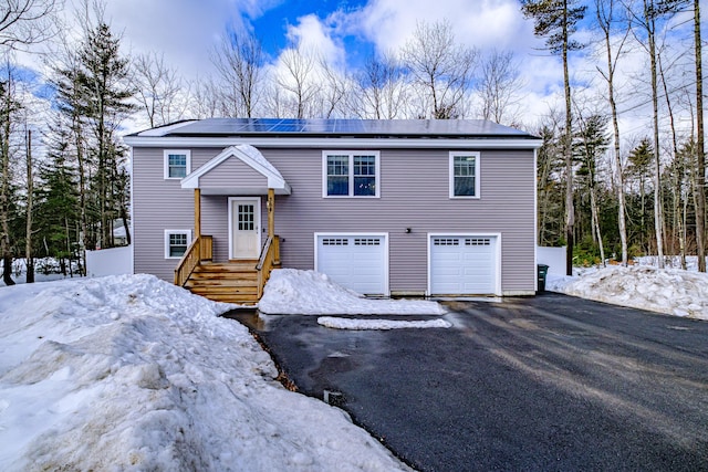 bi-level home featuring driveway, an attached garage, and roof mounted solar panels