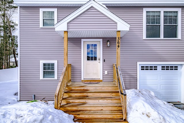 snow covered property entrance featuring an attached garage