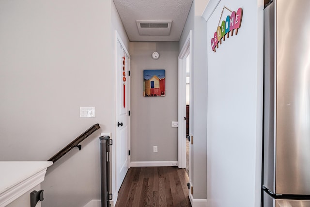 hall featuring a textured ceiling, dark wood-type flooring, an upstairs landing, visible vents, and baseboards