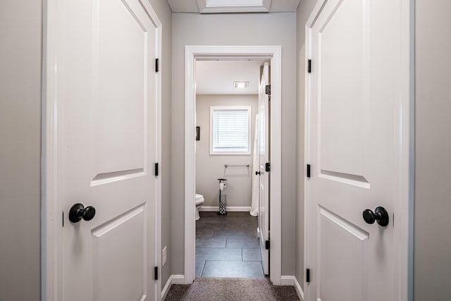 hall featuring baseboards, dark carpet, and dark tile patterned flooring