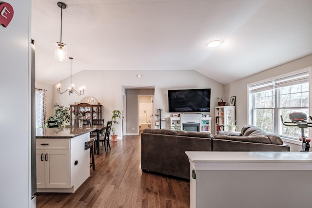 living area with a notable chandelier, vaulted ceiling, and dark wood finished floors