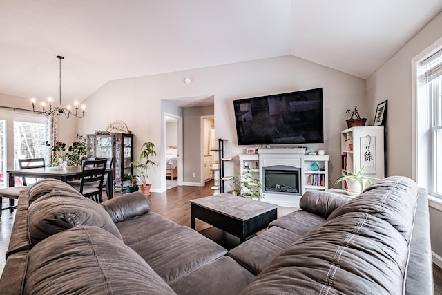 living room with baseboards, lofted ceiling, wood finished floors, a fireplace, and a notable chandelier