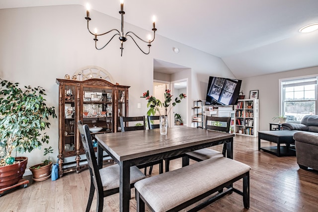 dining area featuring light wood finished floors, vaulted ceiling, and a notable chandelier