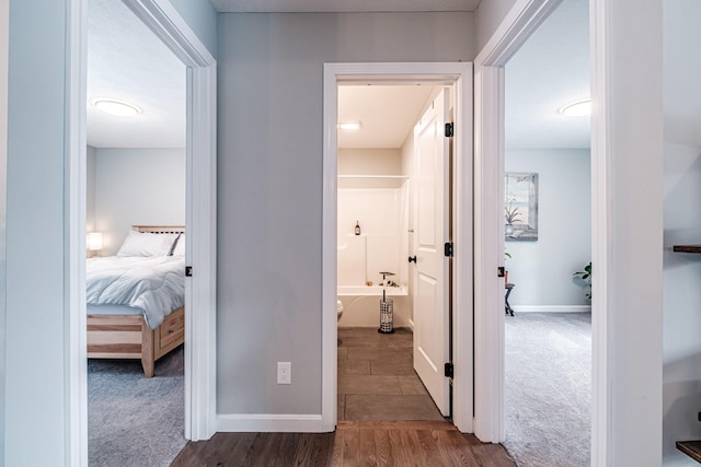 corridor with dark carpet, dark wood finished floors, and baseboards