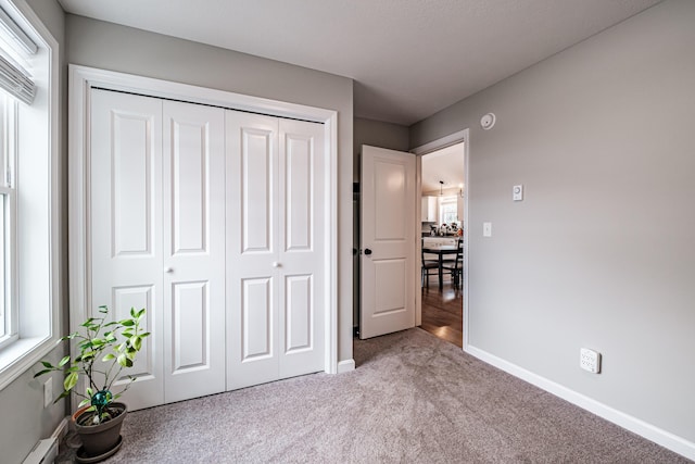 unfurnished bedroom featuring carpet floors, baseboards, a baseboard heating unit, and a closet