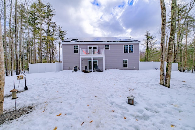 snow covered back of property featuring roof mounted solar panels and fence