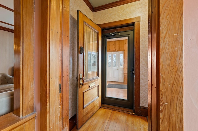 doorway to outside featuring wallpapered walls, crown molding, and light wood finished floors