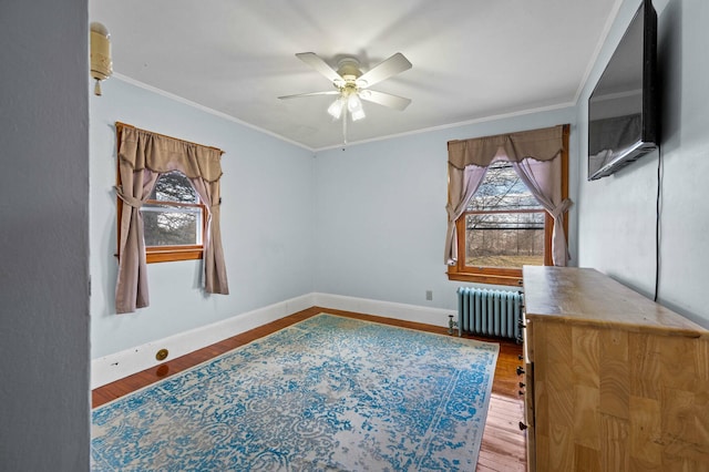 interior space featuring crown molding, baseboards, ceiling fan, radiator heating unit, and wood finished floors