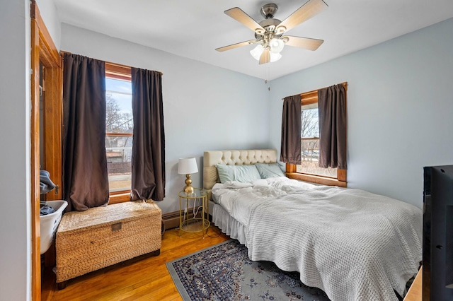 bedroom featuring a ceiling fan, a baseboard heating unit, and wood finished floors