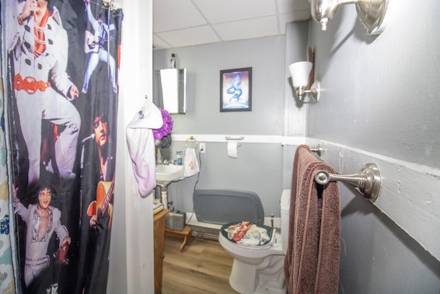 full bath with toilet, a shower with curtain, a drop ceiling, and wood finished floors