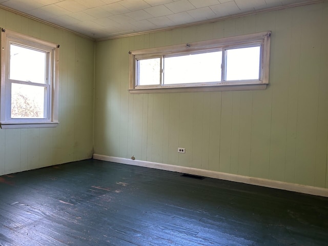 empty room with hardwood / wood-style flooring, visible vents, and baseboards