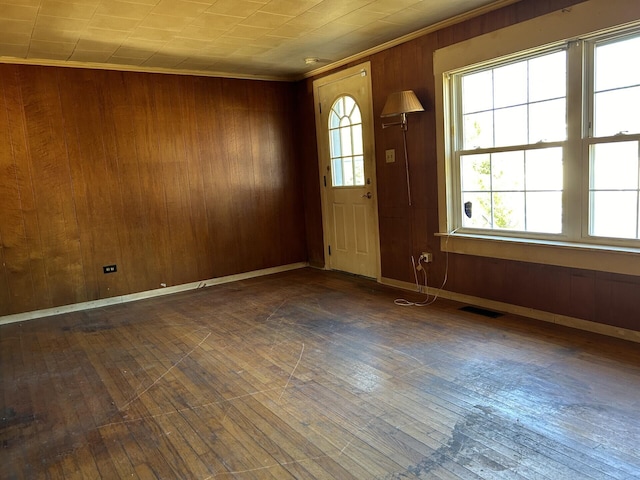 foyer entrance featuring hardwood / wood-style floors, wood walls, visible vents, and crown molding