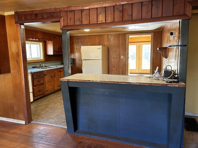 kitchen with wooden walls, brown cabinetry, freestanding refrigerator, light countertops, and crown molding