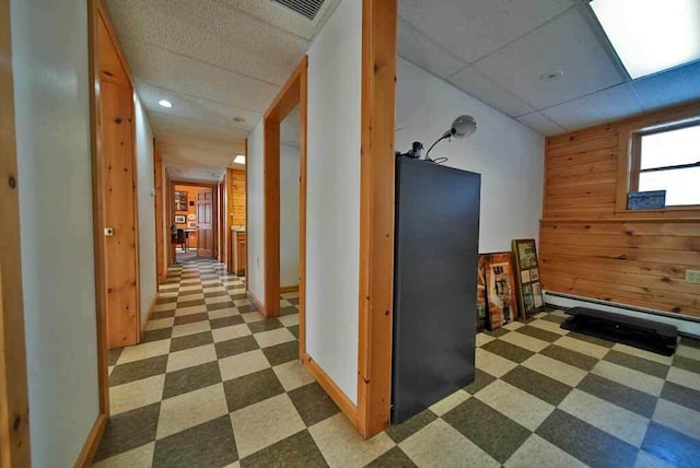 hallway featuring a paneled ceiling, visible vents, baseboard heating, wood walls, and tile patterned floors