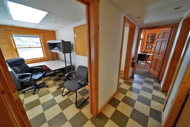 office featuring wood walls, baseboards, a drop ceiling, and tile patterned floors